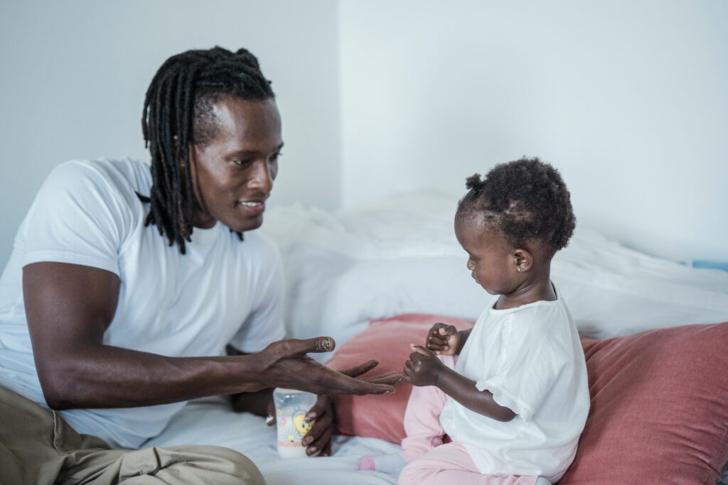 Father and young child sharing a playful moment on the bed, both wearing white shirts.