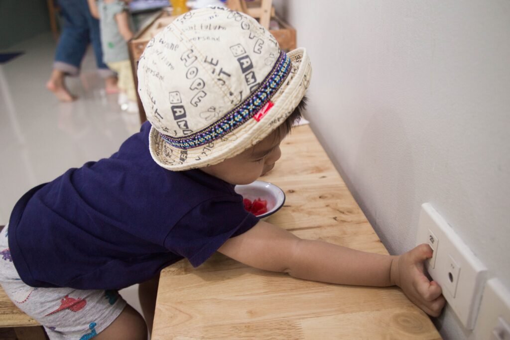 Gestures and Communication Development Young child in hat reaching for an electric socket, highlighting safety concerns for kids indoors.