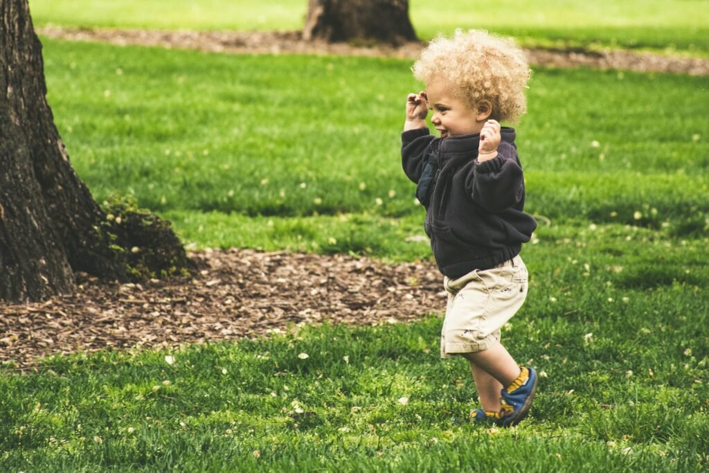 Why Some Children Walk on Their Toes: When Is It Just a Phase and When Should Parents Be Concerned? A happy toddler with curly hair joyfully runs on grass in a sunny park.