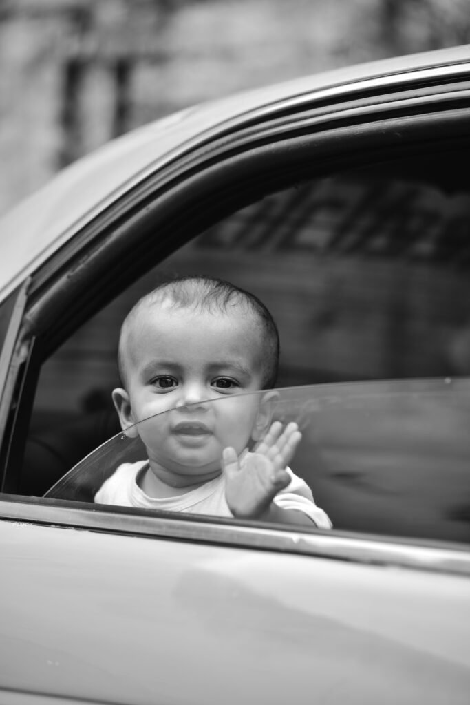 Gestures and Communication Development A cute baby waves from a car window, captured in a striking black and white image.
