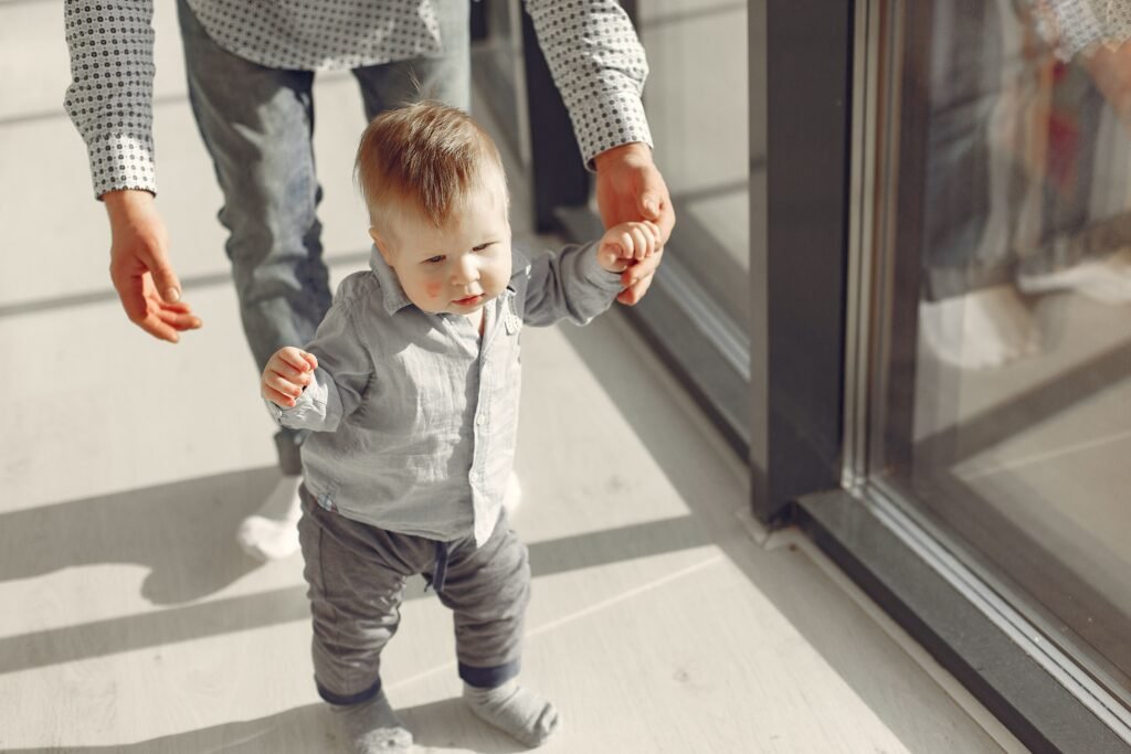 Why Some Children Walk on Their Toes: When Is It Just a Phase and When Should Parents Be Concerned? A toddler learning to walk with support from a parent in a sunlit indoor space.