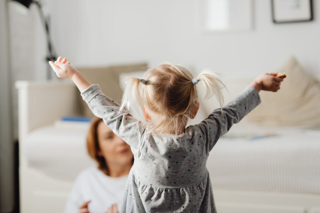 Gestures and Communication Development Cute child with raised arms indoors at home in a playful moment.