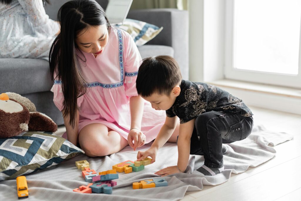 How Parents May Unintentionally Slow Down Therapy Progress (Insights from SensoryCare Therapy Services) An Asian mother and son enjoy quality time together playing with colorful toys on the floor.