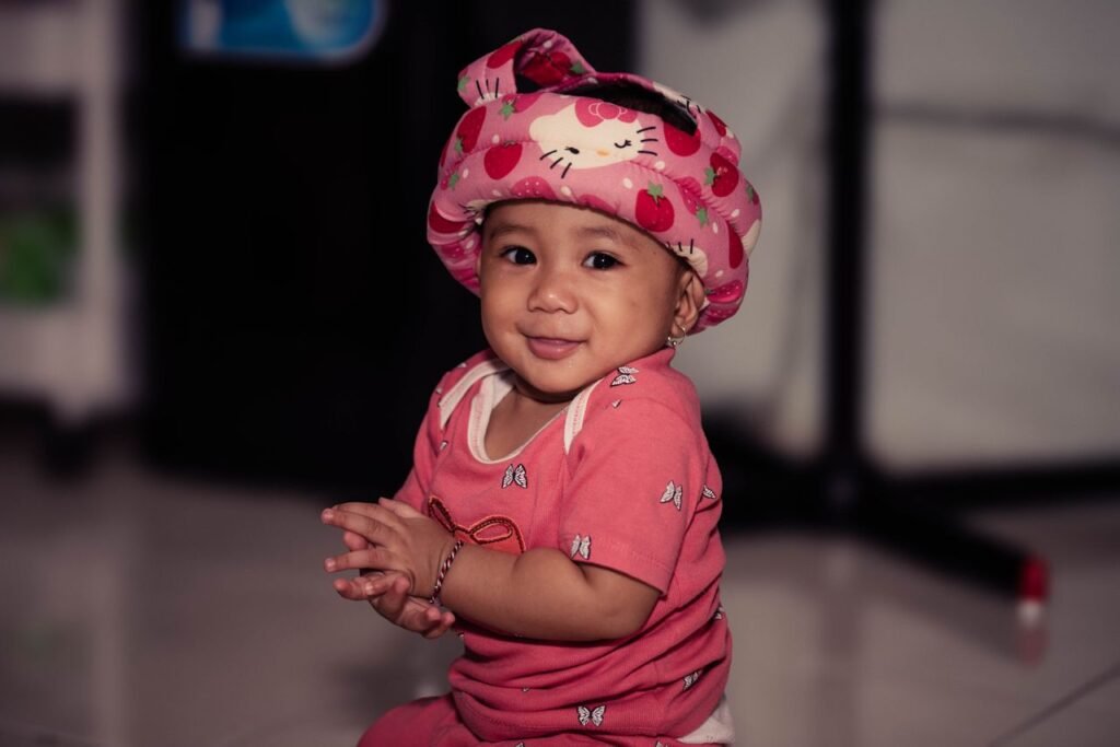 Charming baby smiling while wearing a playful pink hat and outfit, captured indoors.