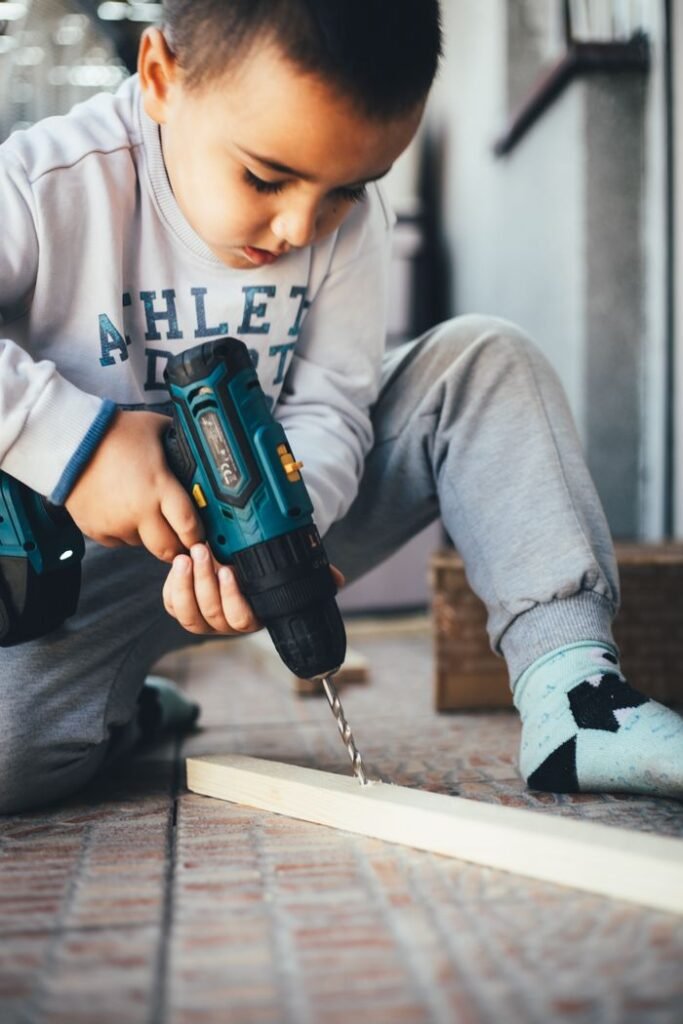 How to improve a child’s attention span A young boy uses an electric drill on a wooden piece, showcasing early skills development.