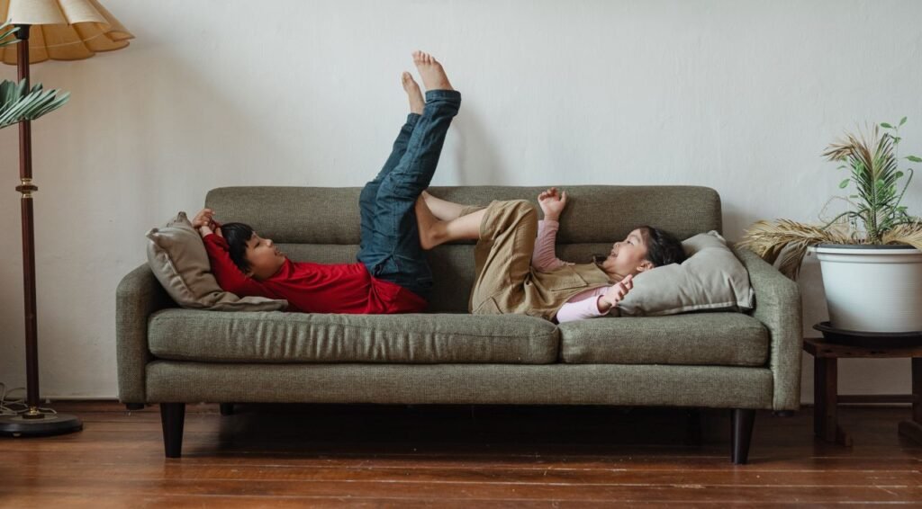 Full body barefoot Asian brother and sister lying on cozy sofa while spending free time in modern living room during weekend