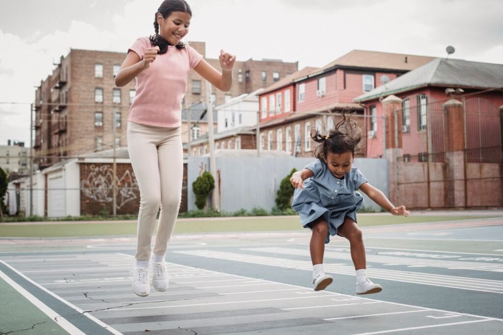 Two young girls joyfully jumping on a playground in an urban setting, showcasing childhood fun and energy.