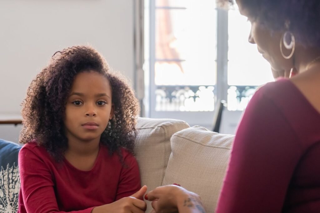 A mother and daughter share a quiet moment sitting together on a couch indoors.