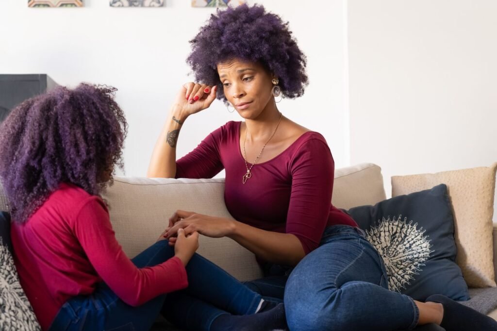 Mother and daughter with purple hair holding hands on the couch, sharing a moment of bonding and connection.