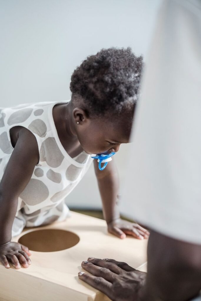 5 DEVELOPMENTAL SIGNS PARENTS SHOULDN’T IGNORE A young child with a pacifier plays on a wooden surface with a parent nearby.