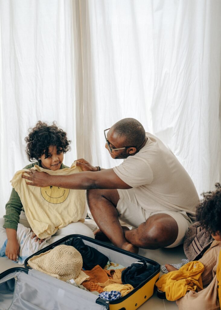 Why Parents Must Stop Doing Everything for Their Child From above of happy African American young father and teen daughter choosing clothes while packing luggage sitting on floor at home