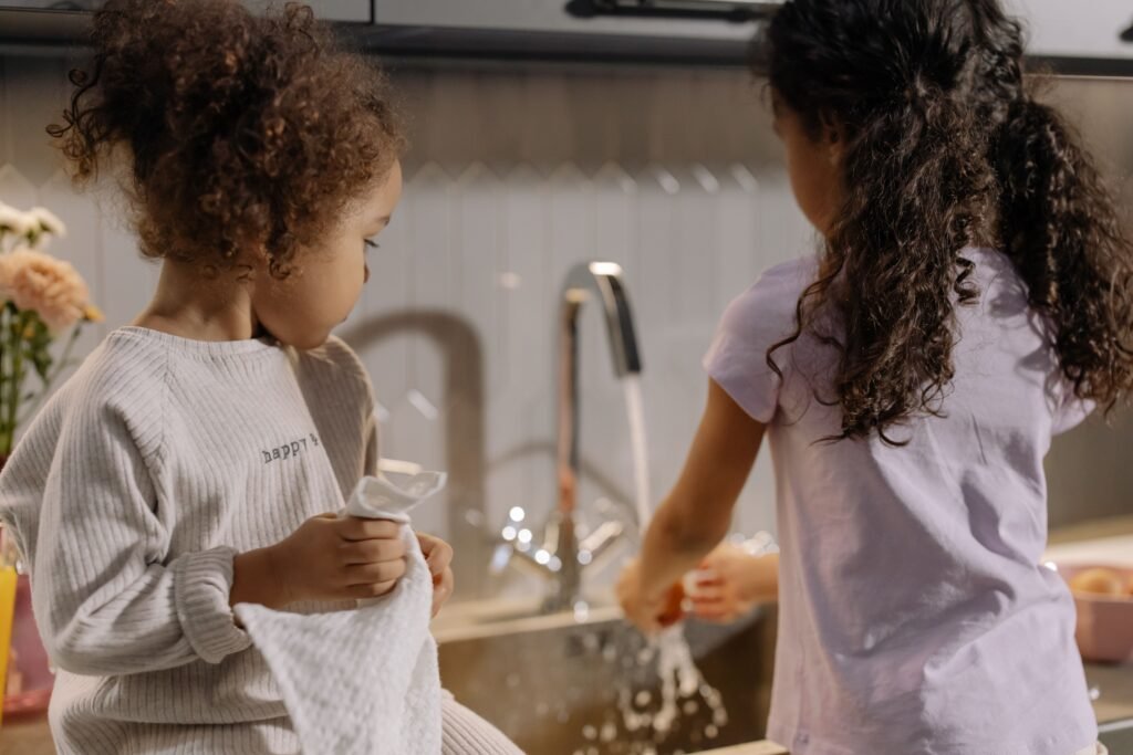 Two young girls washing dishes together in a cozy kitchen setting.