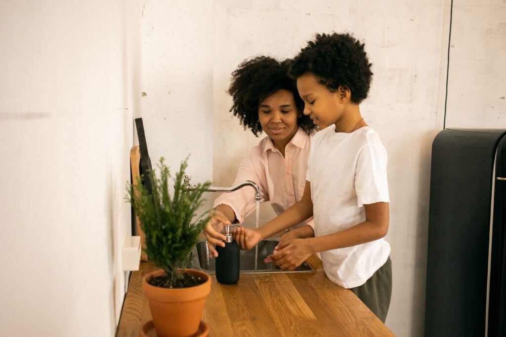 Why Parents Must Stop Doing Everything for Their Child Glad African American mother with son applying soap on hands while washing hands near counter with green potted plant at home
