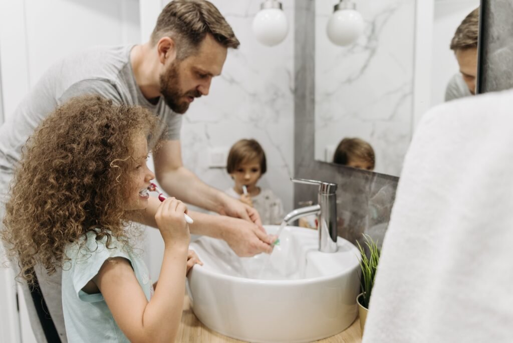Why Parents Must Stop Doing Everything for Their Child Father and children enjoying morning dental routine by brushing teeth together in elegant bathroom.